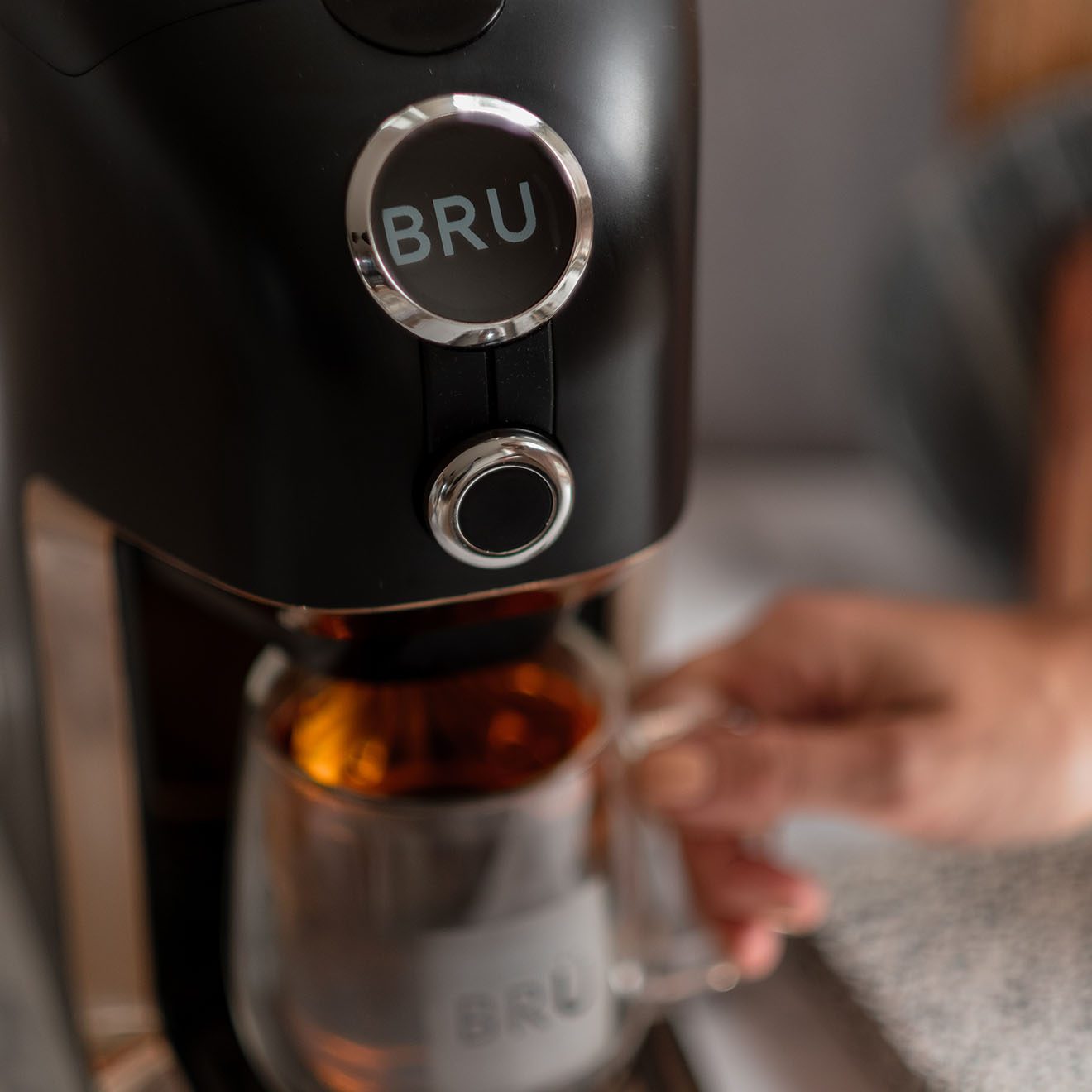Woman taking a brewed cup of tea from the BRU machine.